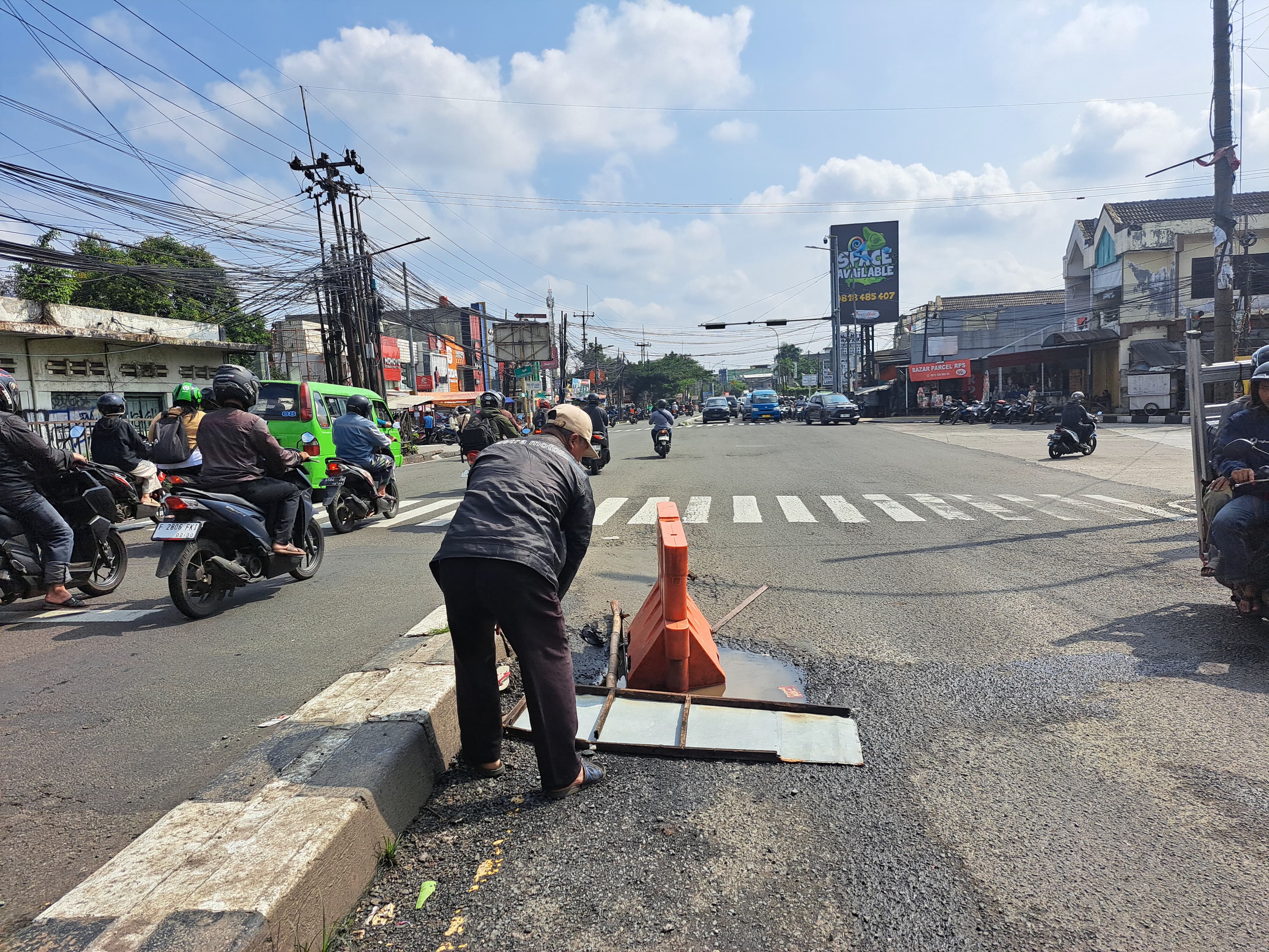 Seorang warga menutup lubang di Jalan Raya Bogor, Kecamatan Bogor Utara dengan water barrier dan plang besi pada Senin (3/3/2025).
