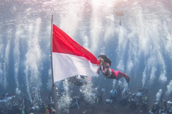 Momen Gubernur Maluku Utara Sherly Tjoanda mengibarkan bendera di dalam laut.