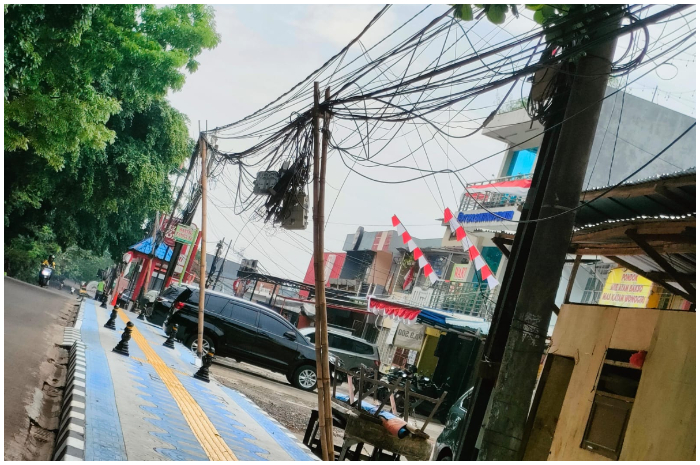 Kabel utilitas menjuntai di atas trotoar Jalan Proklamasi Kota Depok diganjal bambu