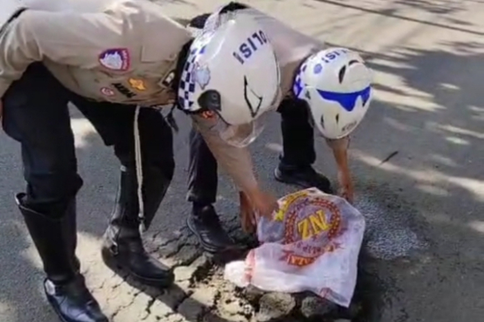 Anggota Unit Lalu Lintas Polsek Tanah Sareal menambal darurat lubang di Jalan Sholeh Iskandar.