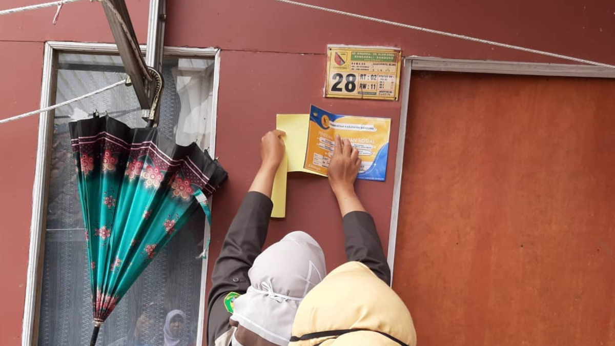 Ilustrasi petugas sedang memasang stiker bansos PKH BPNT di rumah KPM.