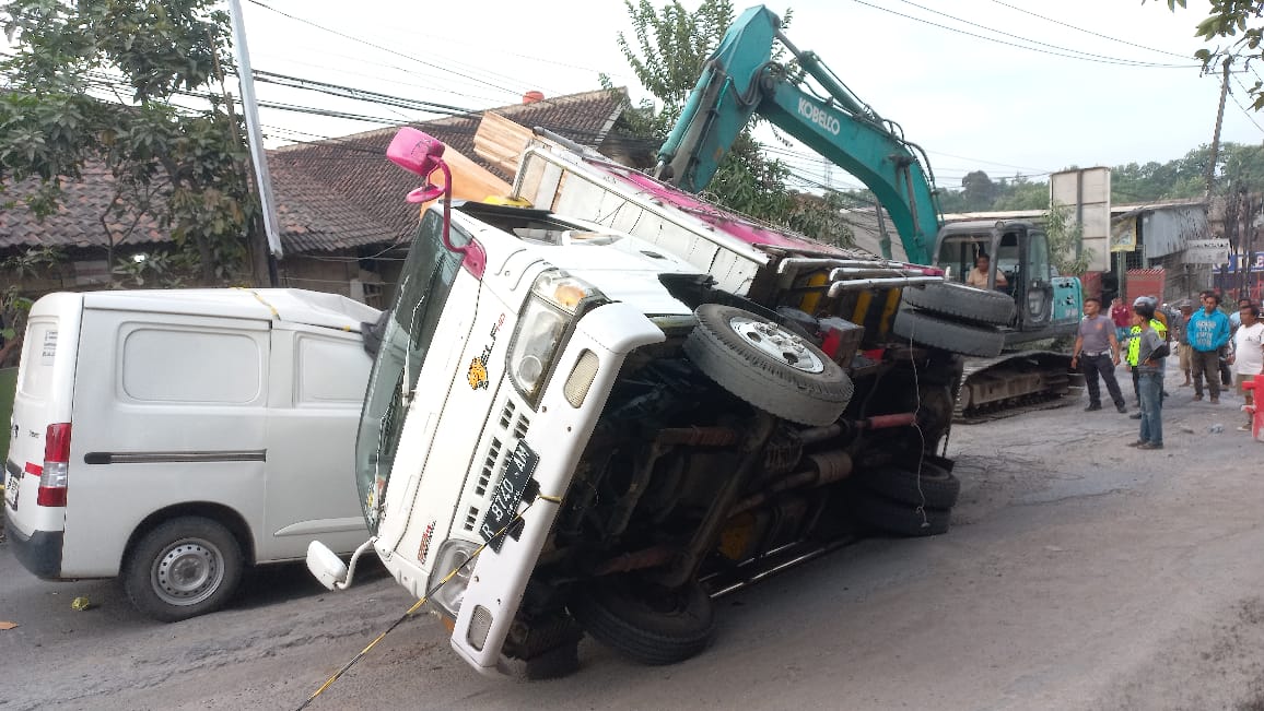 Kondisi truk bermuatan triplek yang mengalami kecelakaan dan terguling menimpa satu unit mobil minibus di Jalan Raya Moh Toha Parung Panjang, Kabupaten Bogor, Rabu 26 November 2025.