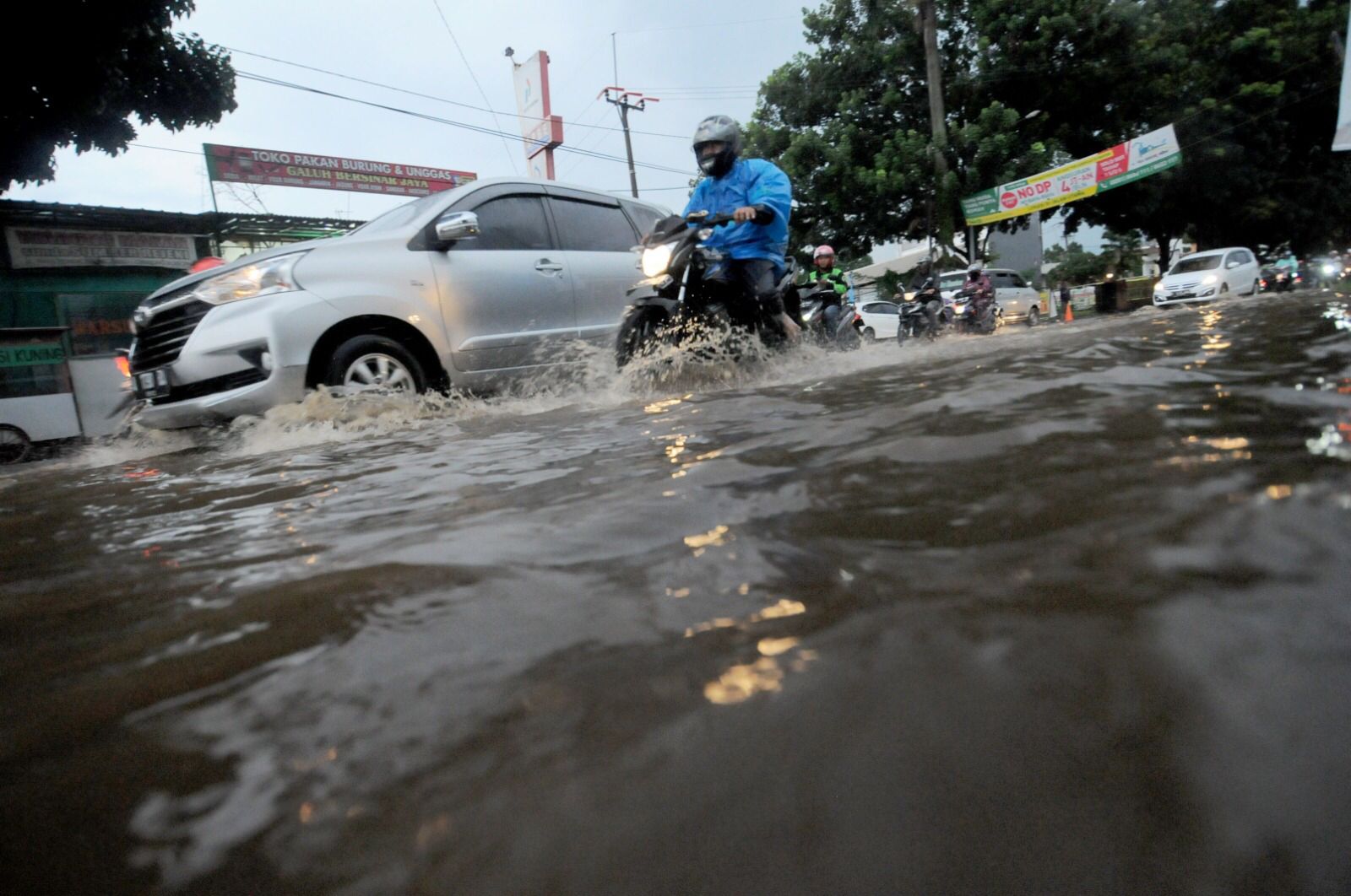 Pengendara menggunakan jas hujan melintas digenangan air akibat hujan deras di Jalan Kedung Halang, Kota Bogor.