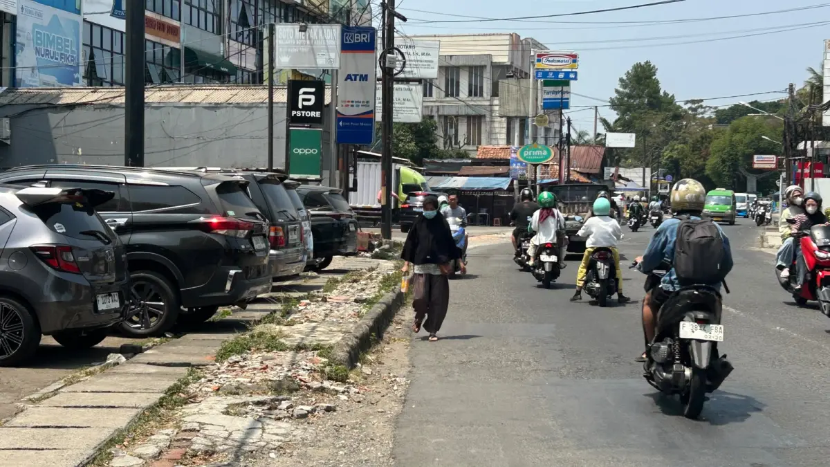 Pejalan kaki yang harus berjalan ke bahu jalan karena area pedestrian di Jalan Sumeru Kota Bogor rusak parah. (Foto : Raissa/Magang Radar Bogor)