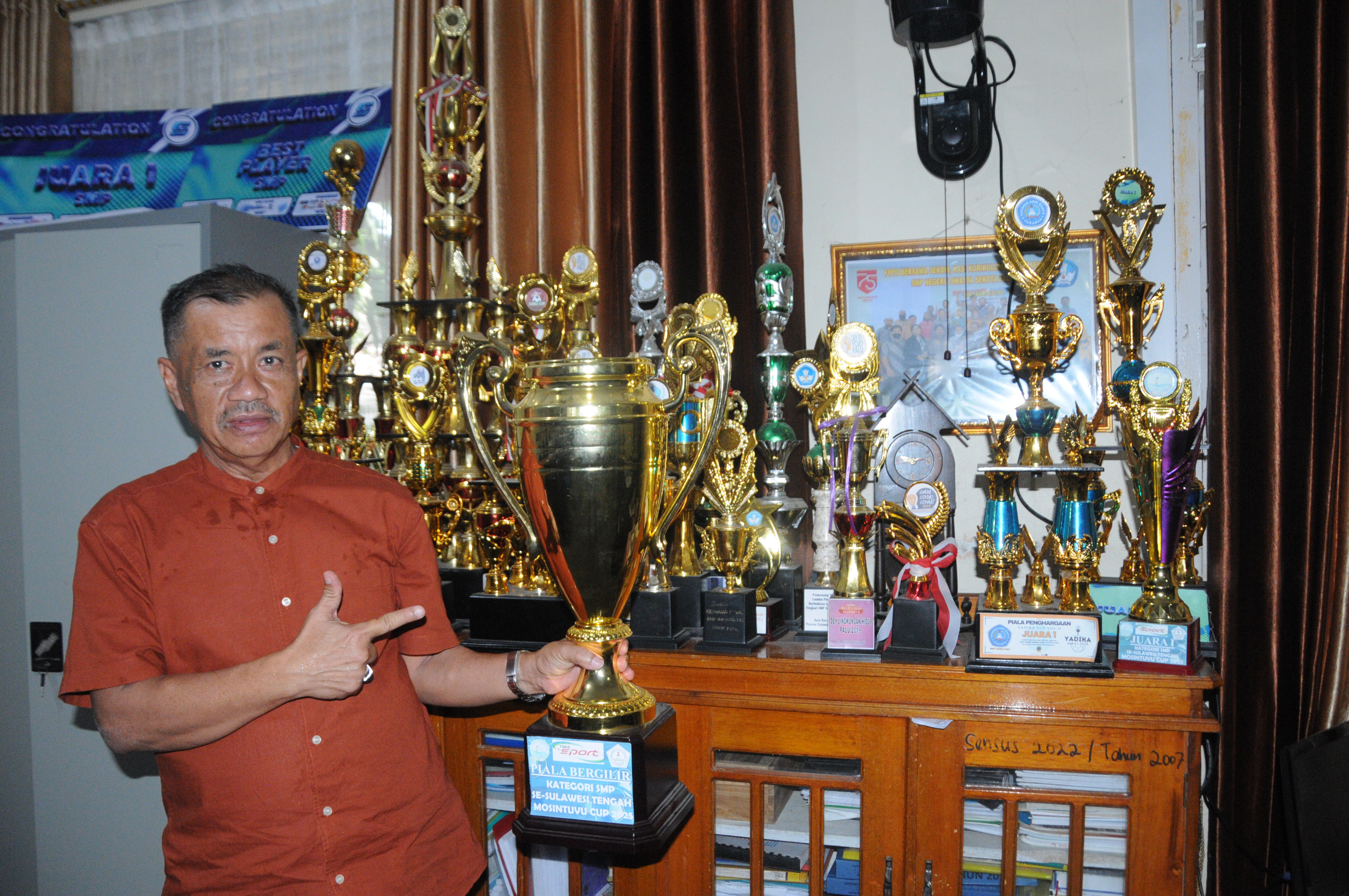 MEMBANGGAKAN : Kepala SMP Negeri 15 Palu, Hilmi SPd MPd bersama sederet piala dari prestasi anak didiknya, Jumat (19/9/2025).