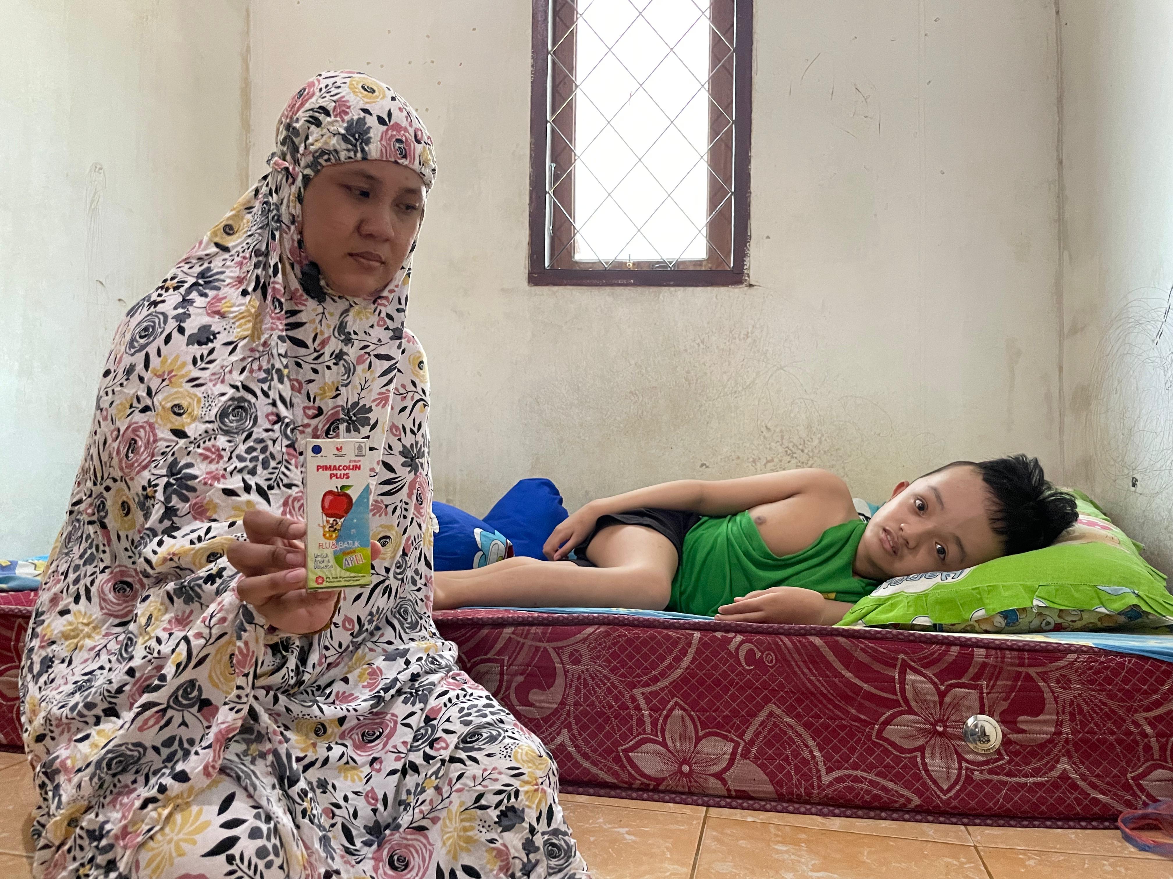 OBAT SATU-SATUNYA: Shintia (26) memegang obat Pimacolin Plus Sirup 60 rasa apel ml, yang menjadi satu-satunya obat andalannya untuk mengobati Amin (8) jika terserang demam pada Kamis (25/9/2025).