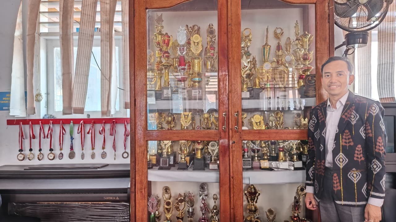 BERPRESTASI: &lrm;Kepala SDN 15 Palu, Yusuf berfoto di lemari yang penuh dengan piala pencapaian prestasi sekolah yang dipimpinnya.