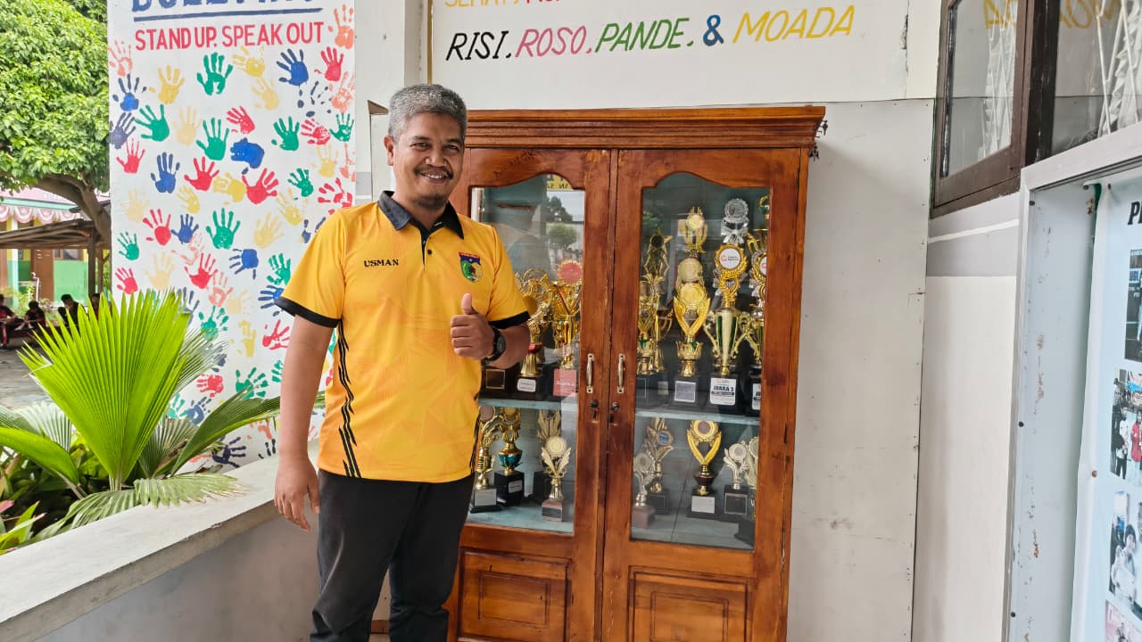 JAGA PRESTASI: Kepala SDN Inpres 4 Birobuli, Usman berfoto di depan lemari pajangan sekolahnya. Tampak deretan piala yang menandakan raihan prestasi sekolahnya.