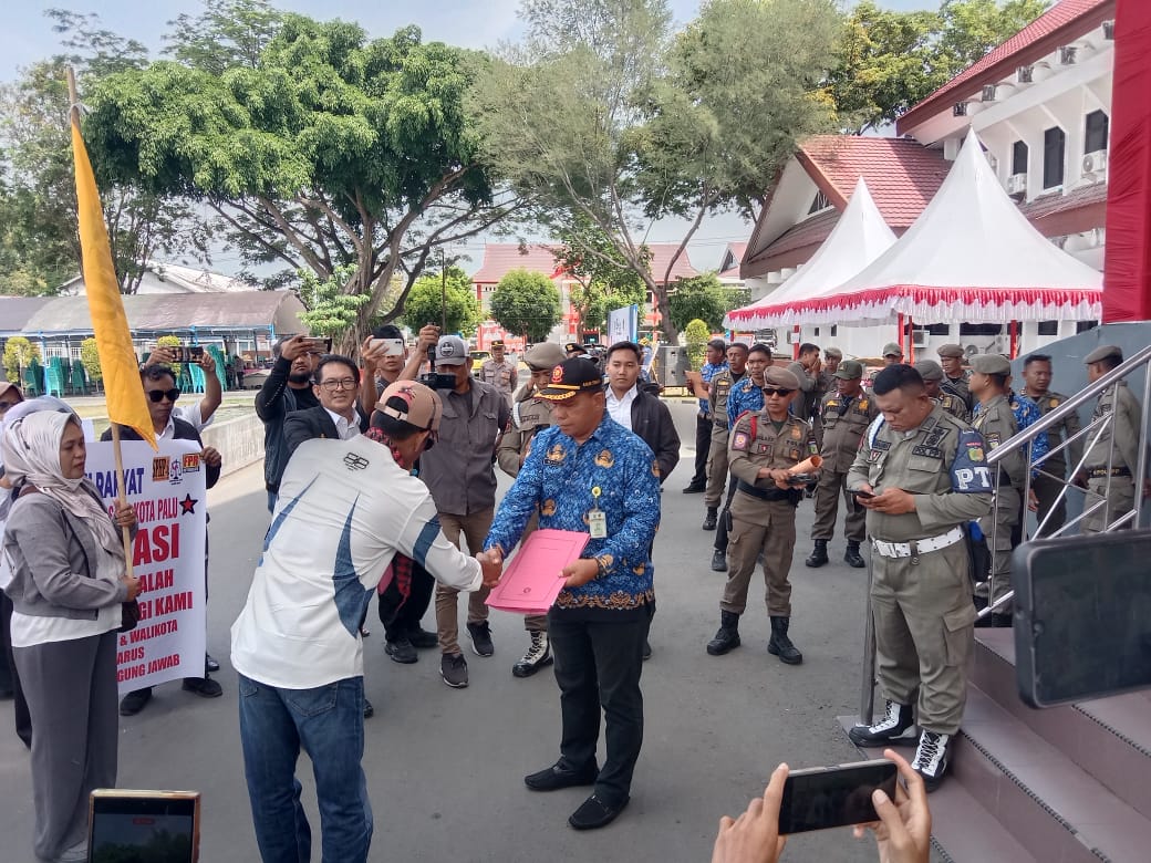 PEMKOT DISOMASI : Ratusan tenaga honorer Kota Palu membentangkan spanduk tuntutan di halaman Kantor Wali Kota Palu, Senin (1/12/2025), saat menyerahkan somasi kepada Pemerintah Kota Palu.