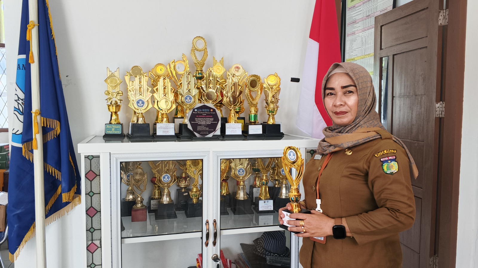 ISTIMEWA: Plt Kepala SDN Lasoani, Elvira SPd MPd menunjukkan piala terbaru yang diraih oleh sekolah pada saat berpose di lemari piala dan berfoto di ruangan kelas pada Senin (08/12/2025).