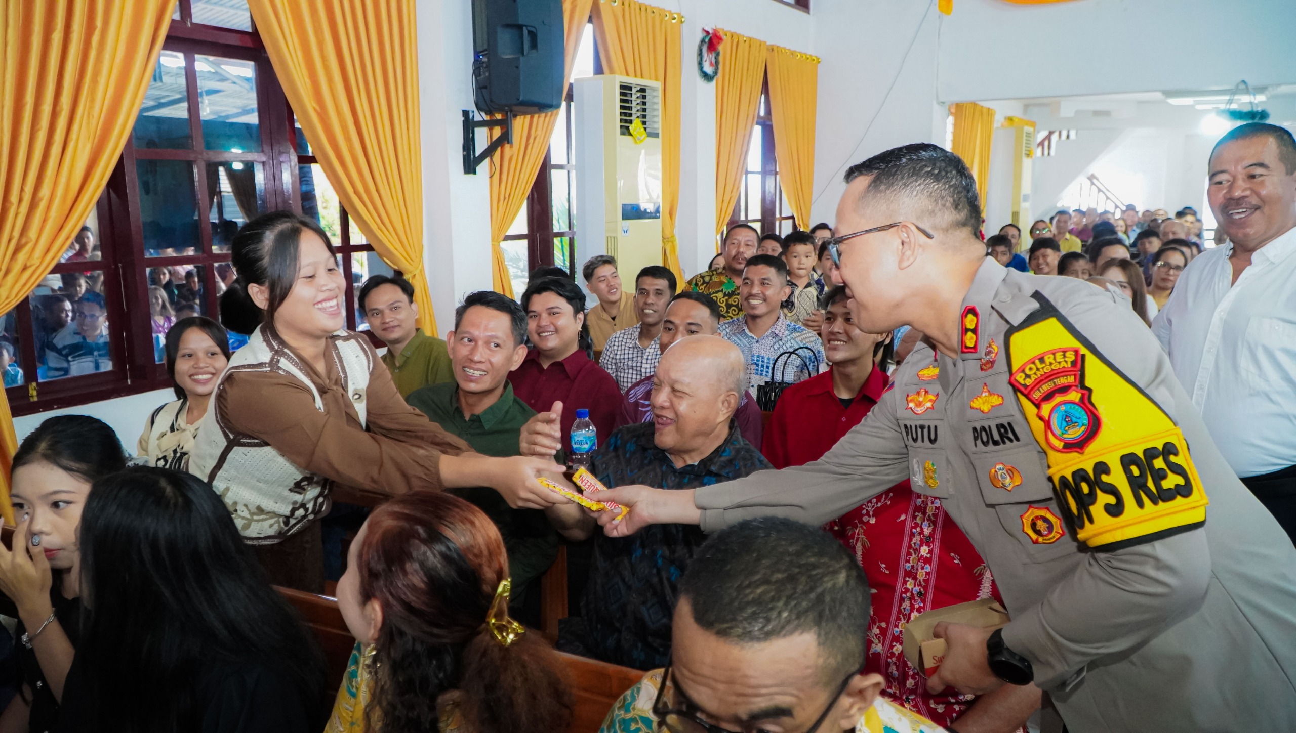 COKLAT: Kapolres Banggai, AKBP Putu Hendra Bingkari membagikan coklat kepada salah satu jemaat yang sedang melaksanakan ibadah perayaan Natal, Kamis (25/12/2025).(FOTO: NENDRA PRASETYA/RADAR PALU).  &nbsp;