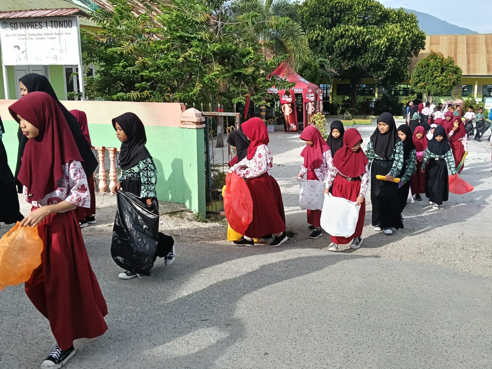 Siswa SD Inpres 1 Tondo membawa kantong plastik dan karung bekas, menyusuri lingkungan sekitar sekolah demi lingkungan bersih dan sehat.