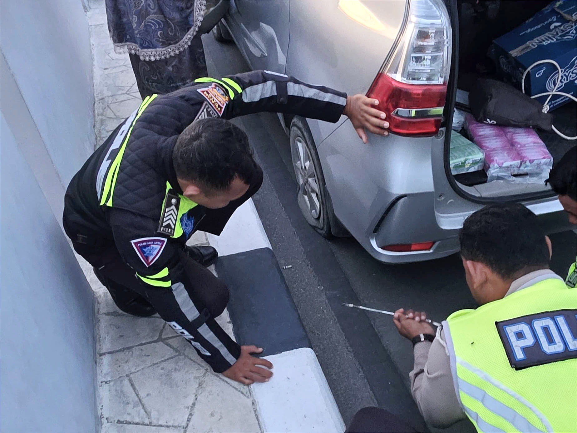 Petugas Satlantas Polresta Palu membantu pengendara mengganti ban mobil yang bocor saat patroli subuh Ramadhan di jalur elevated road Jalan Cumi-Cumi, Kota Palu.
