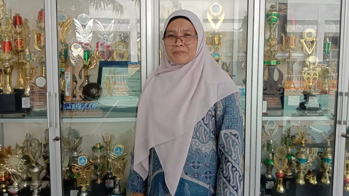 Wakil Kepala Sekolah Bidang Kurikulum SMPN 16 Palu, Mulsifrah, berdiri di depan deretan piala prestasi siswa di sekolah, Kamis (4/6/2026). (ADE SAFITRI/RADAR PALU)