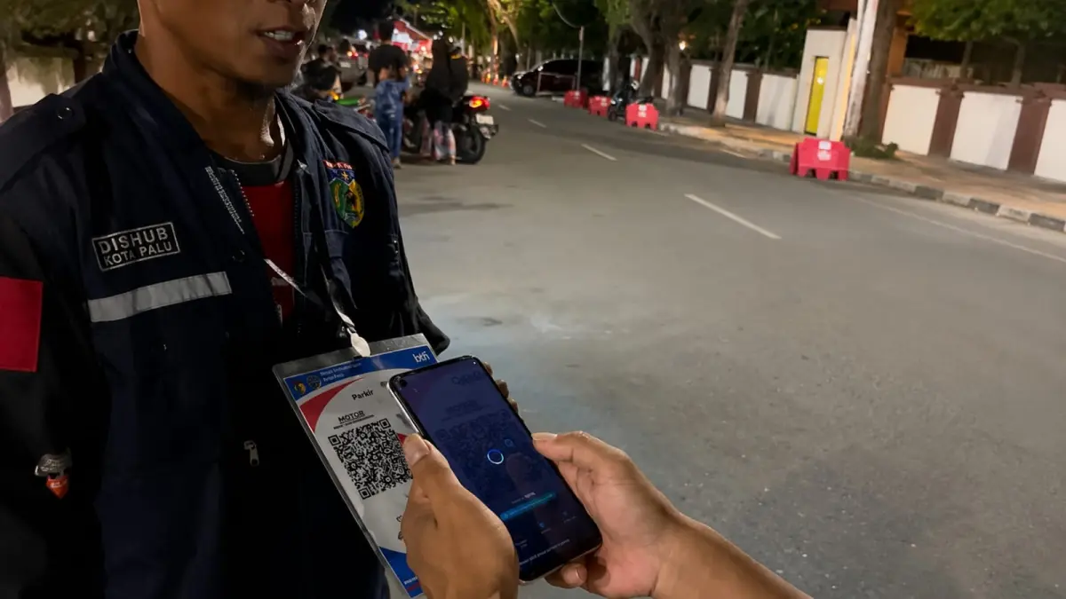 Petugas Dinas Perhubungan Kota Palu melayani pembayaran parkir menggunakan QRIS di kawasan Taman Vatulemo sebagai bagian dari transformasi layanan parkir digital.l. FOTO RAFFY/RADAR PALU&nbsp;