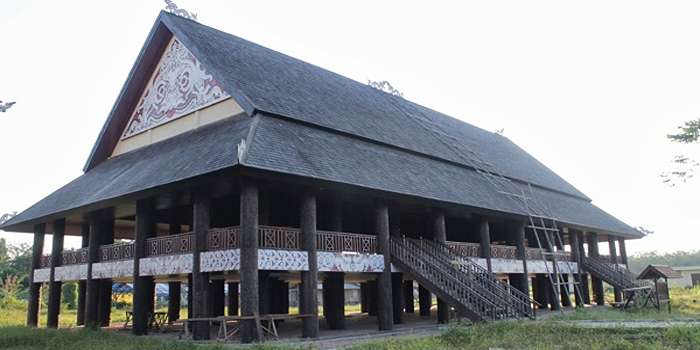 Foto rumah adat Kalimantan Timur, desain rumah panggung kayu ulin penuh ukiran etnik dan warna simbolik, cocok buat inspirasi hunian unik.