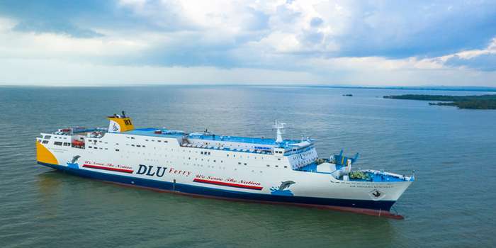 Dharma Kencana VII  dengan latar laut biru dan aktivitas pelayaran.