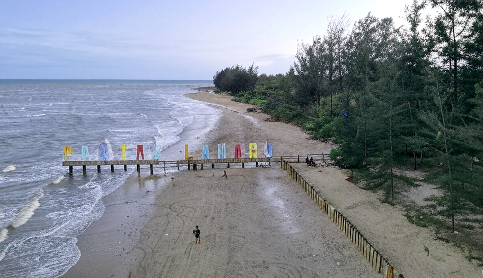 Keindahan Pantai Lamaru Balikpapan dengan pasir putih, pohon cemara, dan suasana teduh yang memikat hati pengunjung.