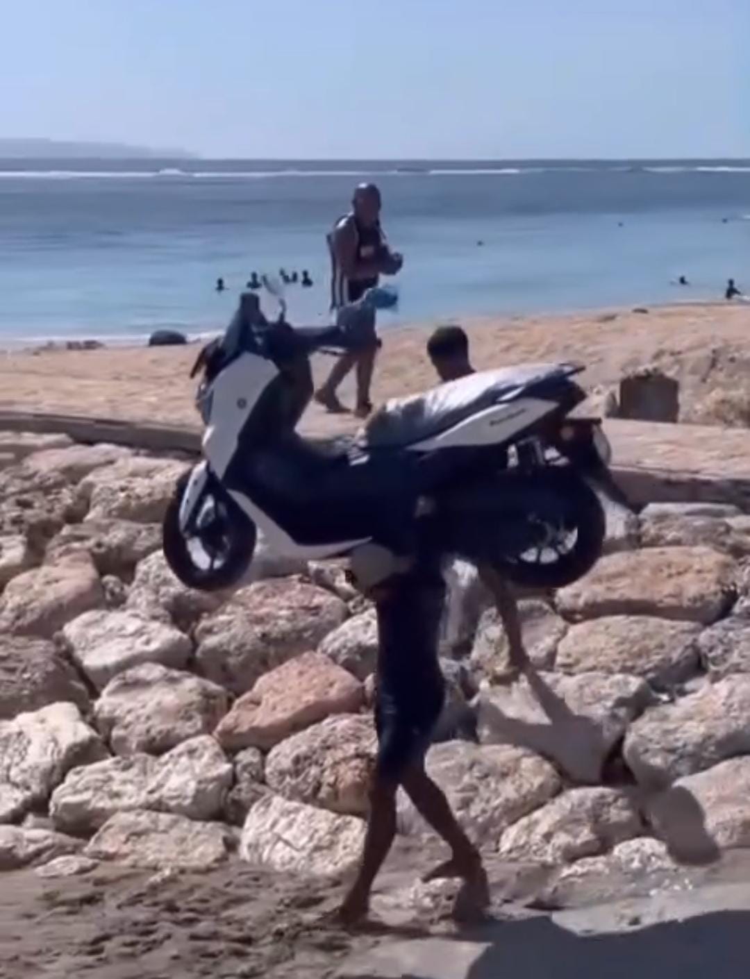 Pria kuat di pantai NTT mengangkat motor menuju kapal di tengah ombak tinggi &mdash; aksi nyata penuh tenaga dan inspirasi.