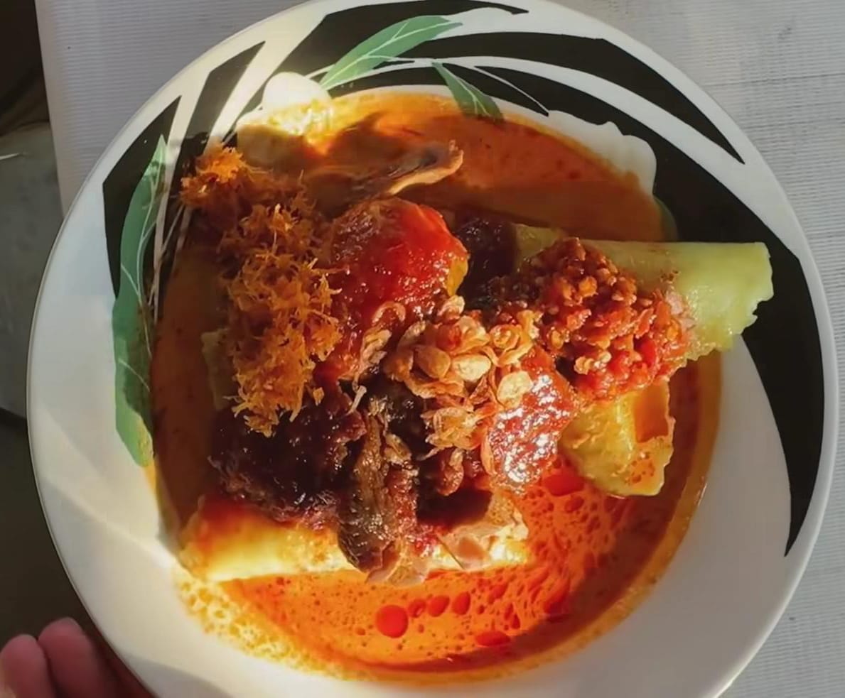 Semangkuk lontong sayur Acil Muslimah berkuah merah gurih, taburan serundeng, dan sambal yang menggoda mata.
