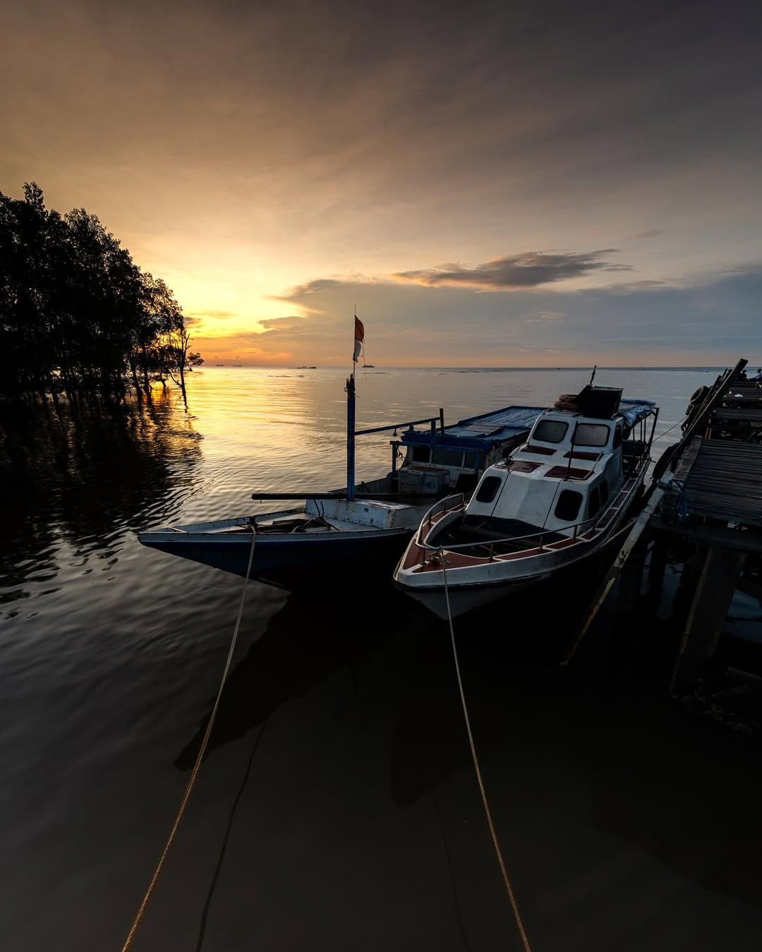 Pemandangan Pantai Kenyamukan saat sore hari&mdash;laut biru berpadu dengan langit jingga, deretan perahu nelayan, dan hutan mangrove di kejauhan.