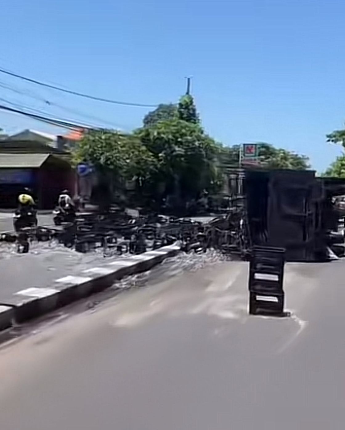 Truk bermuatan minuman terguling di Jalan Ida Bagus Mantra &mdash; visual dramatis botol minuman berserakan di jalan, petugas dan warga berjibaku membersihkan.