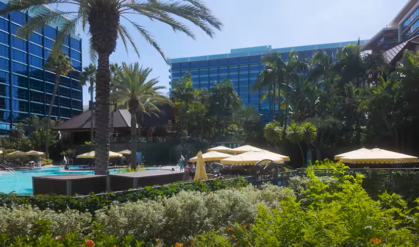 Tampak depan Disneyland Hotel Anaheim dengan kolam tropis dan menara tematik &mdash; simbol kemewahan dan nostalgia Disney.