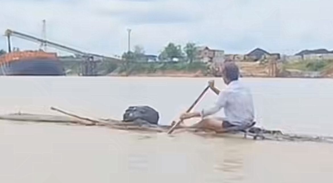 Seorang pria mendayung batang kayu di tengah Sungai Mahakam &mdash; visual dramatis penuh tekad dan harapan.