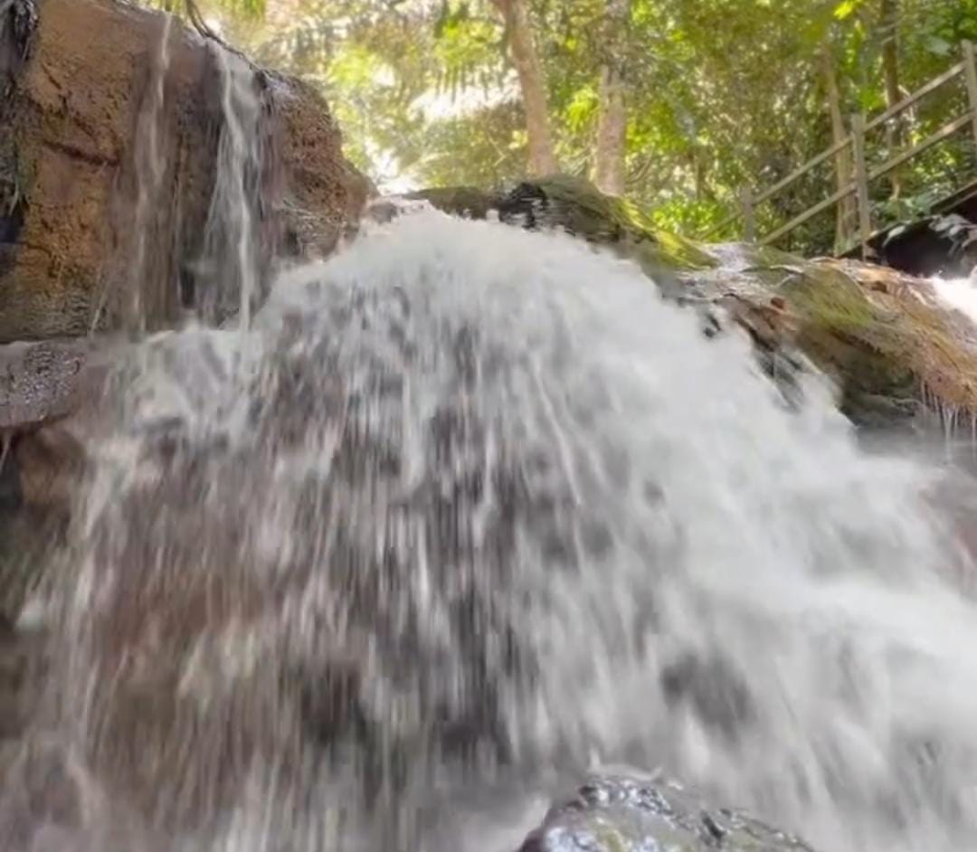 Panorama Air Terjun Pesona Perjiwa yang dikelilingi pepohonan hijau &mdash; visual alami penuh ketenangan dan keindahan.