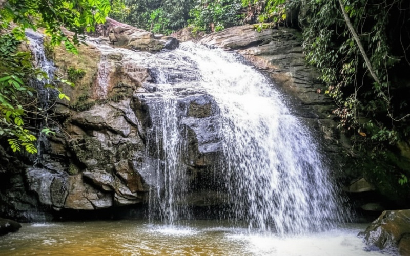 Pemandangan Telaga Permai Batu Besaung dengan air terjun mini dan pepohonan rimbun&mdash;visual alami yang memanjakan mata.