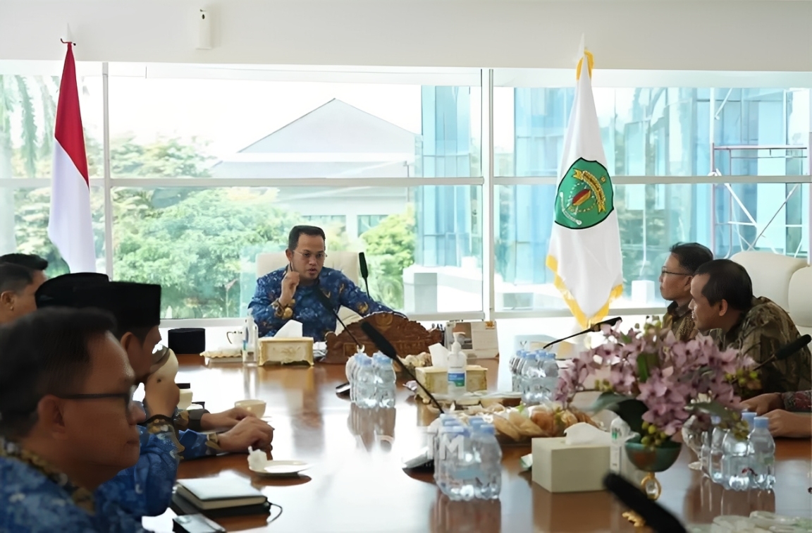Gubernur Harum dan jajaran Telkom berdiskusi dengan latar peta Kaltim dan ilustrasi jaringan digital sebagai simbol konektivitas.