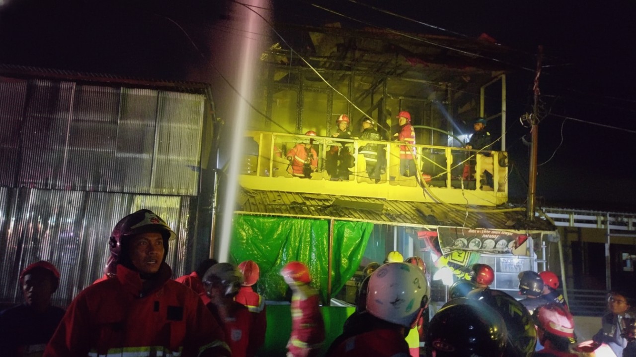 Bangunan dua lantai warung Acil Sindi terbakar dengan api di lantai atas, kepulan asap gelap dan petugas pemadam bekerja intens Cess.