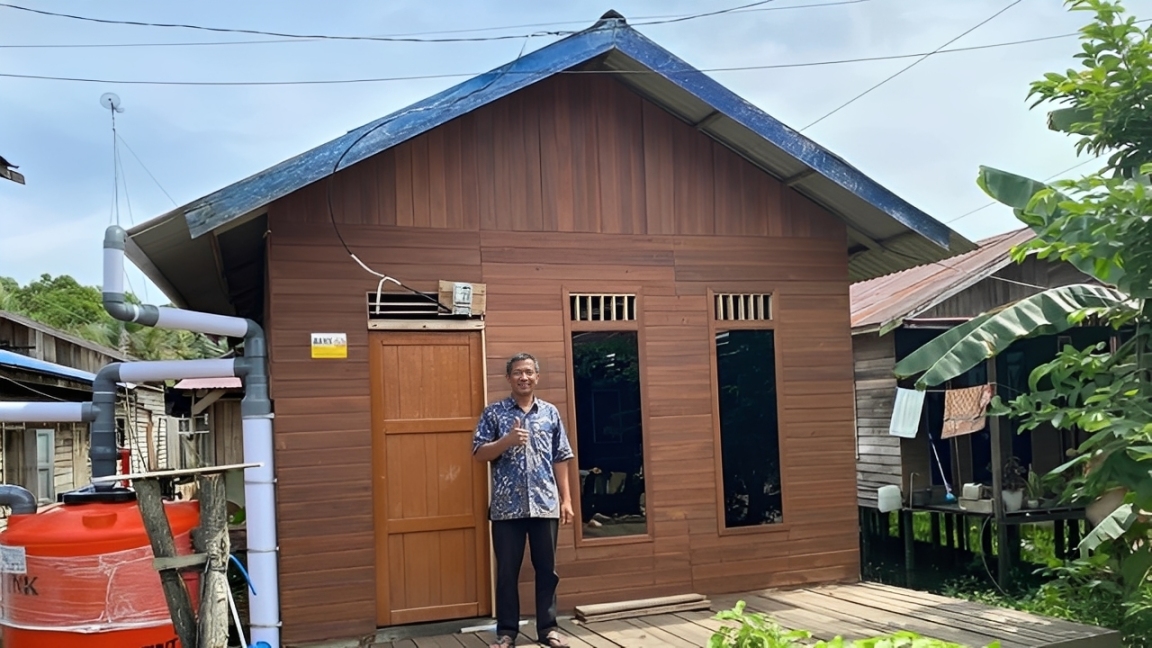 Seorang warga penerima manfaat Program Bantuan Stimulan Perumahan Swadaya (BSPS) 2025 di Kaltim berpose di depan rumahnya yang telah direnovasi.
