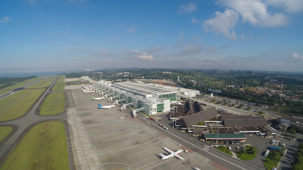 Suasana aktivitas penumpang di Bandara SAMS Sepinggan Balikpapan dengan latar pesawat komersial yang bersiap lepas landas.