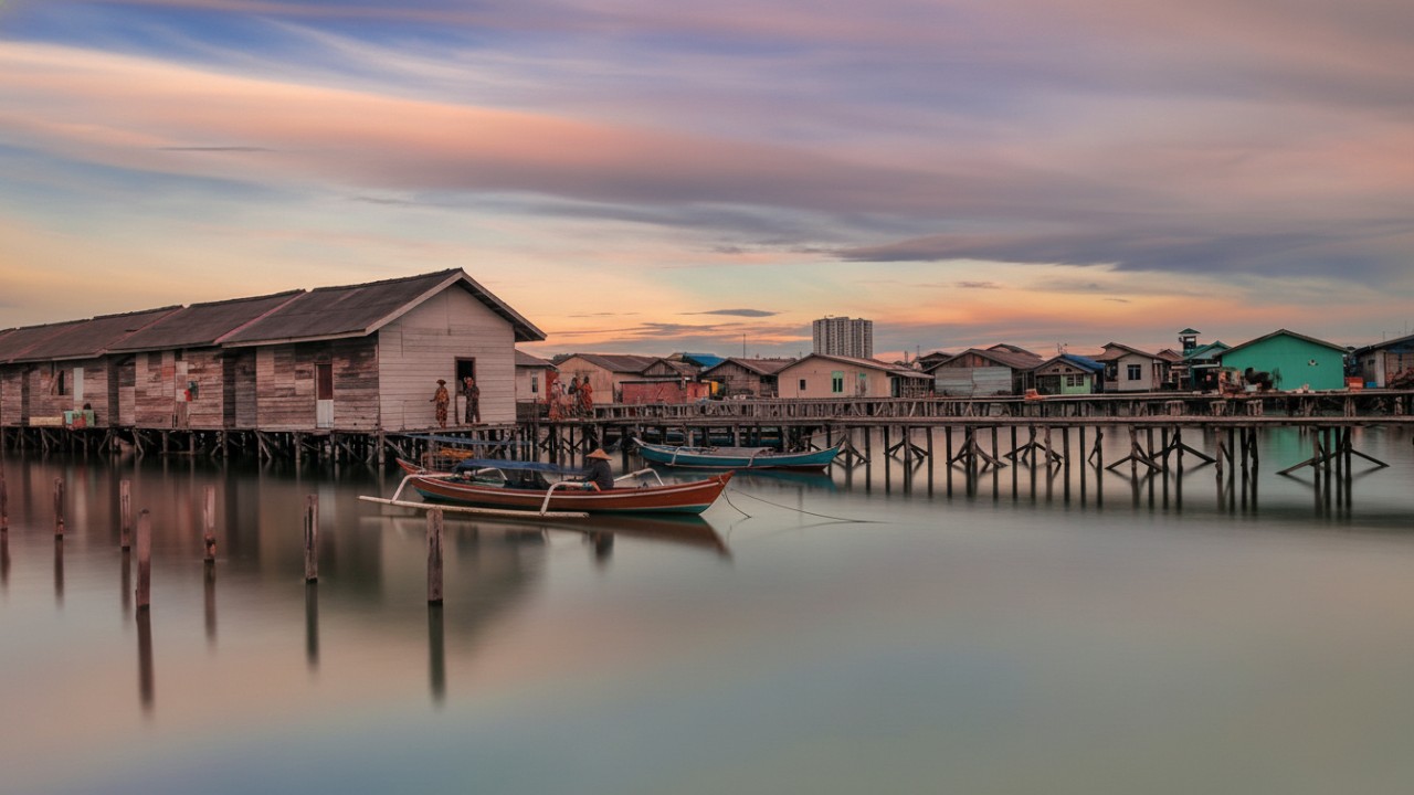 Jembatan kayu Kampung Atas Air Margasari dengan rumah panggung dan laut sebagai latar, suasana sore yang menenangkan.