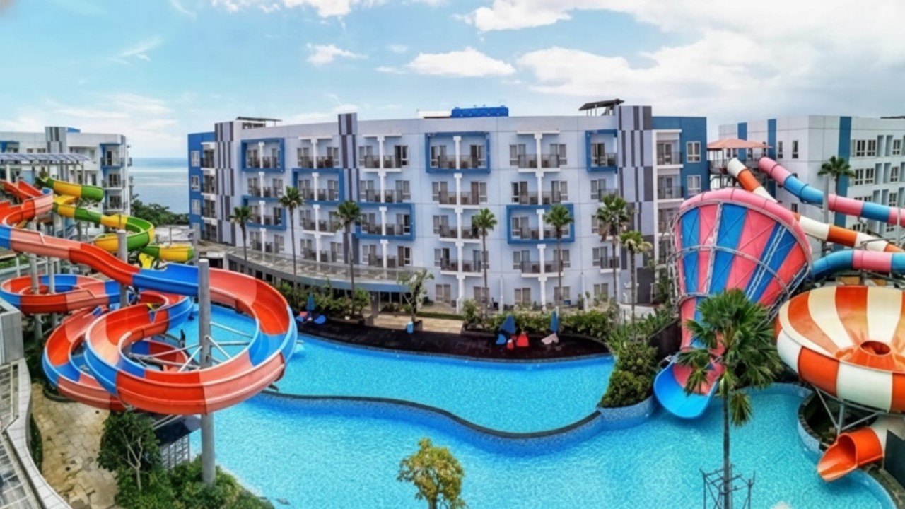 Suasana Aquaboom Waterpark Balikpapan dengan kolam dan seluncuran air berlatar pemandangan kota dari rooftop.