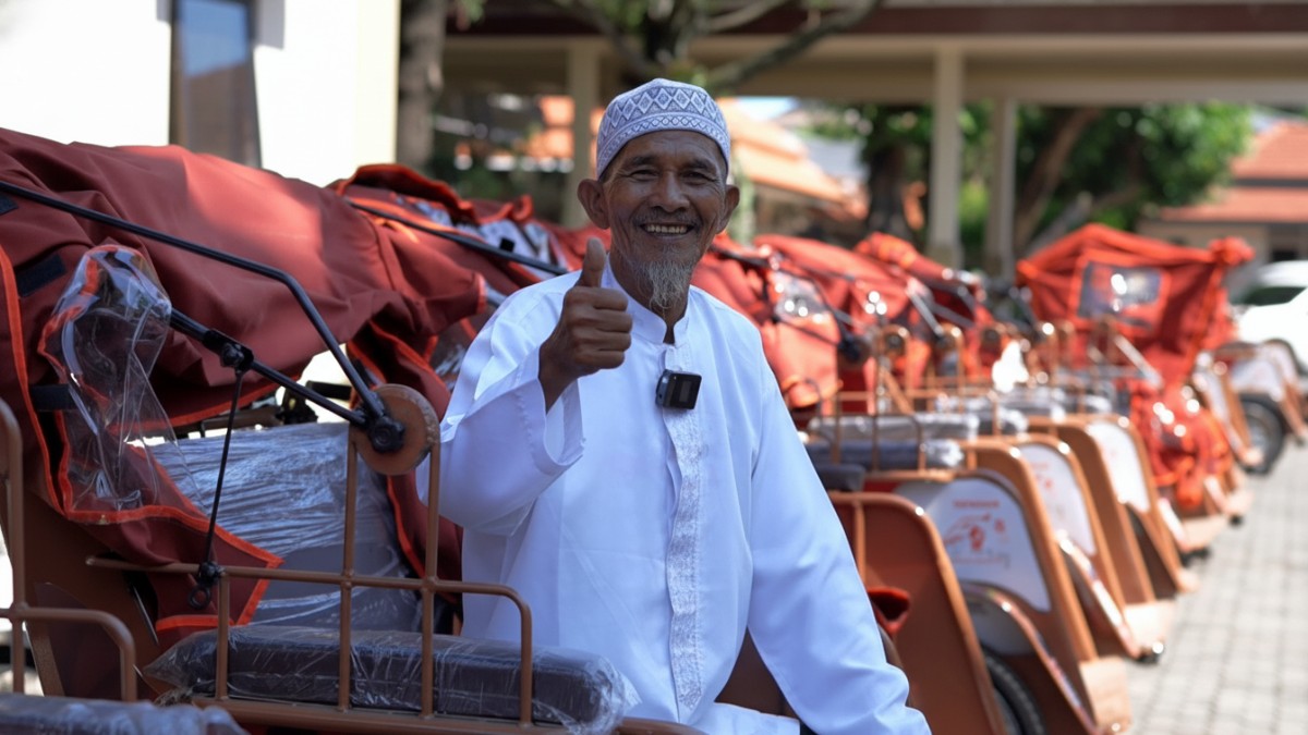 Budi Utomo duduk bahagia di samping becak listrik barunya.
