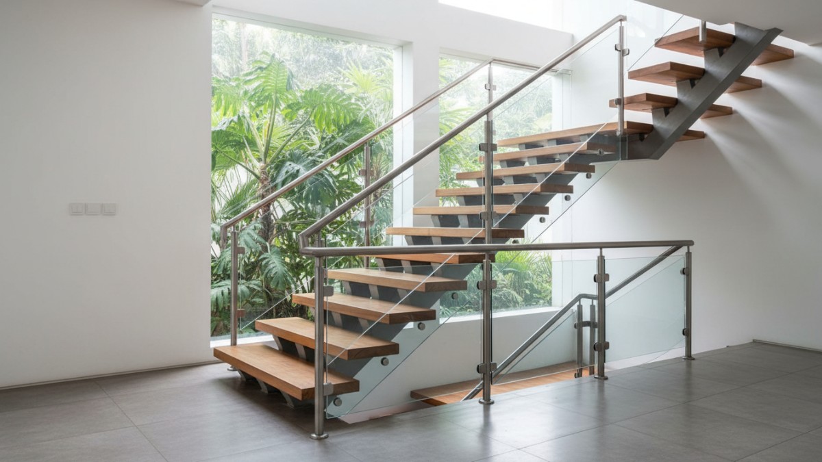 Desain railing tangga modern dengan kombinasi stainless steel dan kaca memperkuat karakter interior rumah minimalis.
