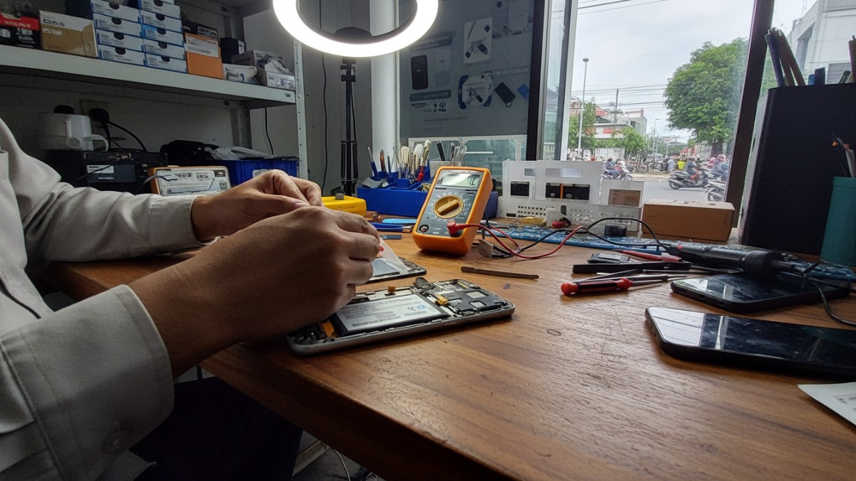 Teknisi memeriksa kondisi baterai smartphone lawas di meja servis.