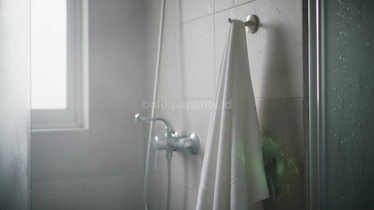 Handuk tergantung di kamar mandi lembap dengan pencahayaan natural, menggambarkan potensi bakteri tersembunyi