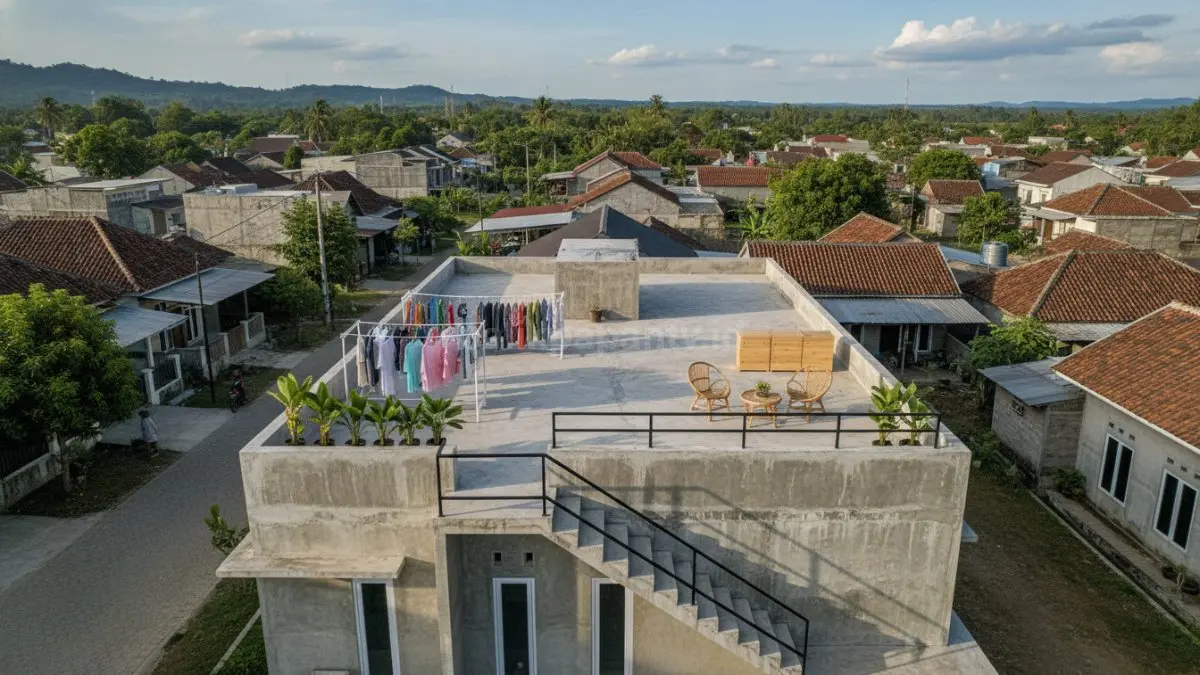 rumah 1 lantai modern di kawasan desa Indonesia yang menampilkan dak jemuran beton di bagian atas bangunan. Area dak digunakan sebagai ruang multifungsi dengan jemuran pakaian yang tertata rapi, serta sebagian ruang difungsikan sebagai tempat penyimpanan ringan dan area santai keluarga pada sore hari. Tampak tangga akses samping yang menghubungkan area bawah dan atas dengan desain sederhana namun aman. Lingkungan sekitar menggambarkan suasana permukiman desa yang berkembang di Kalimantan Timur, memperlihatkan transformasi atap rumah menjadi ruang produktif yang fungsional dan efisien. (BTV/Ai)