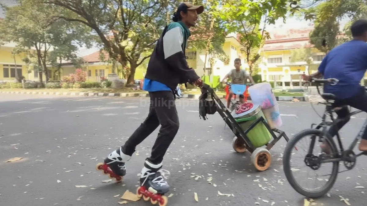 Foto tangkapan layar aksi lincah seorang penjual es krim keliling yang menggunakan sepatu roda saat mendorong gerobaknya di jalan raya.