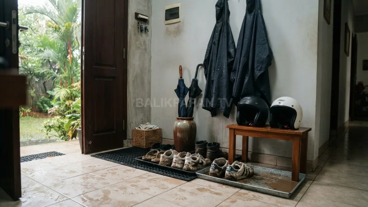 Area ruang kotor rumah tropis dengan sepatu berlumpur, jas hujan basah, payung, helm, serta baki penampung air yang tertata rapi. (BTV/AI)