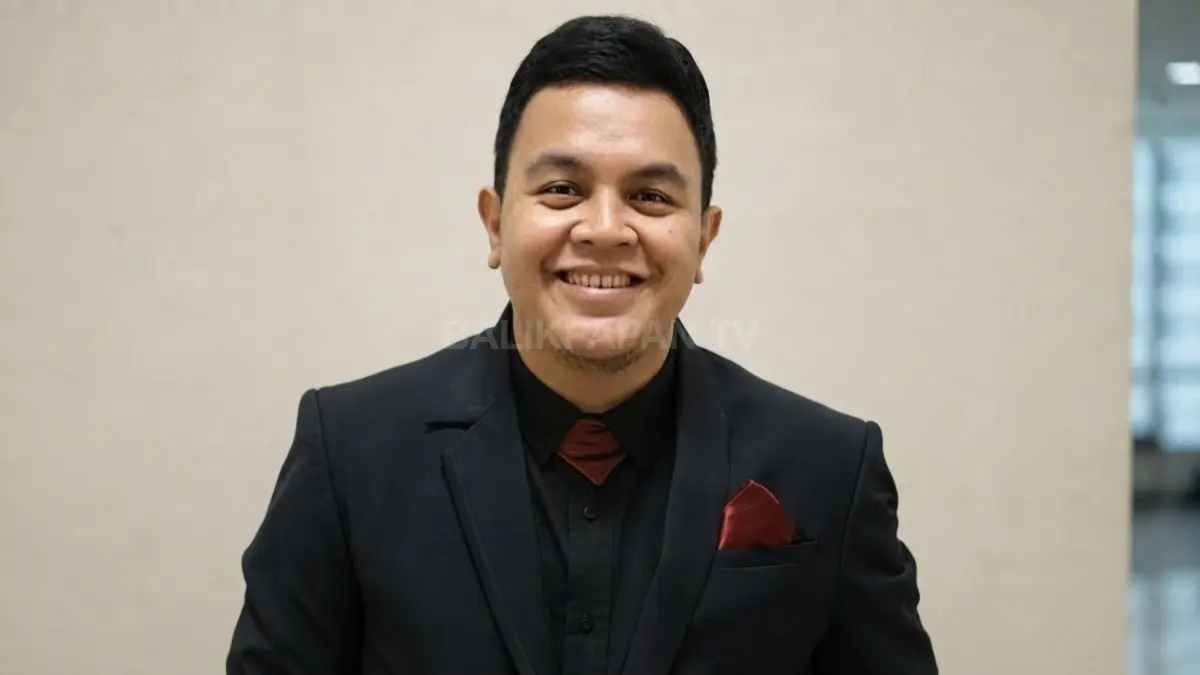 Potret senyum hangat Tulus tampil rapi dalam balutan jas hitam dengan aksen merah. (BTV/Ai)