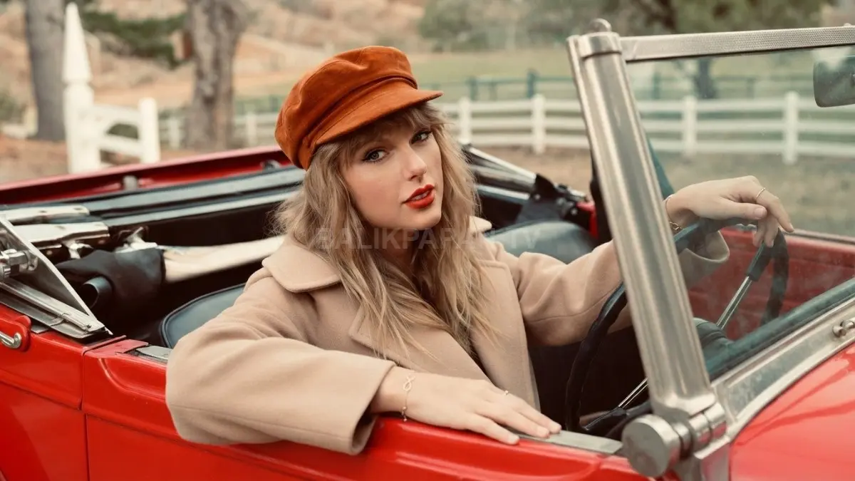 Gaya klasik Taylor Swift mengenakan topi kencur oranye di dalam mobil antik memancarkan nuansa retro yang hangat. (BTV/Ai)