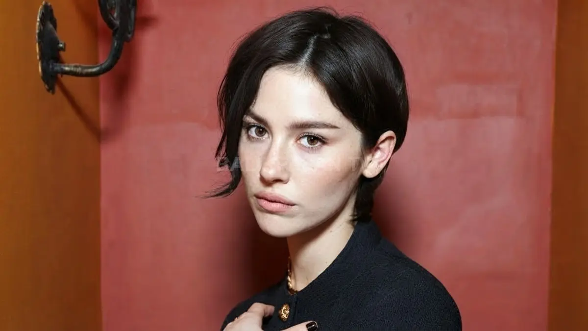Potret elegan Gracie Abrams dengan gaya rambut pendek dan tatapan tajam berlatar dinding bernuansa hangat. (BTV/Ai)