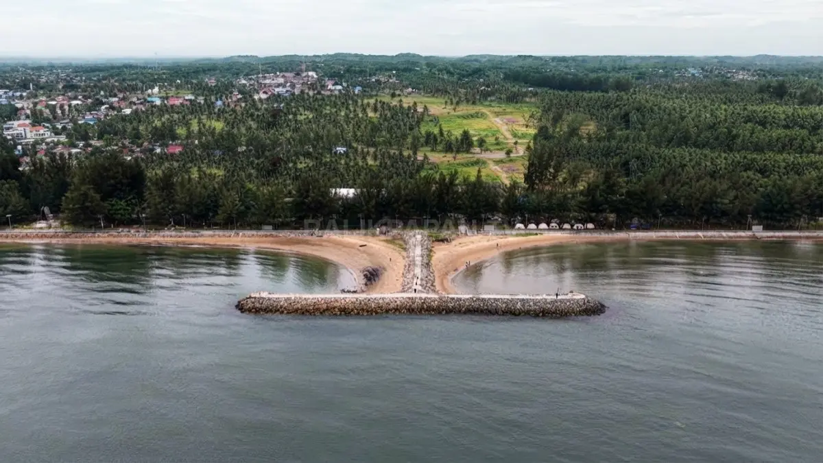 Pantai Manggar Segarasari Balikpapan dengan pasir luas, pepohonan cemara, dan pemecah gelombang di kawasan pesisir.