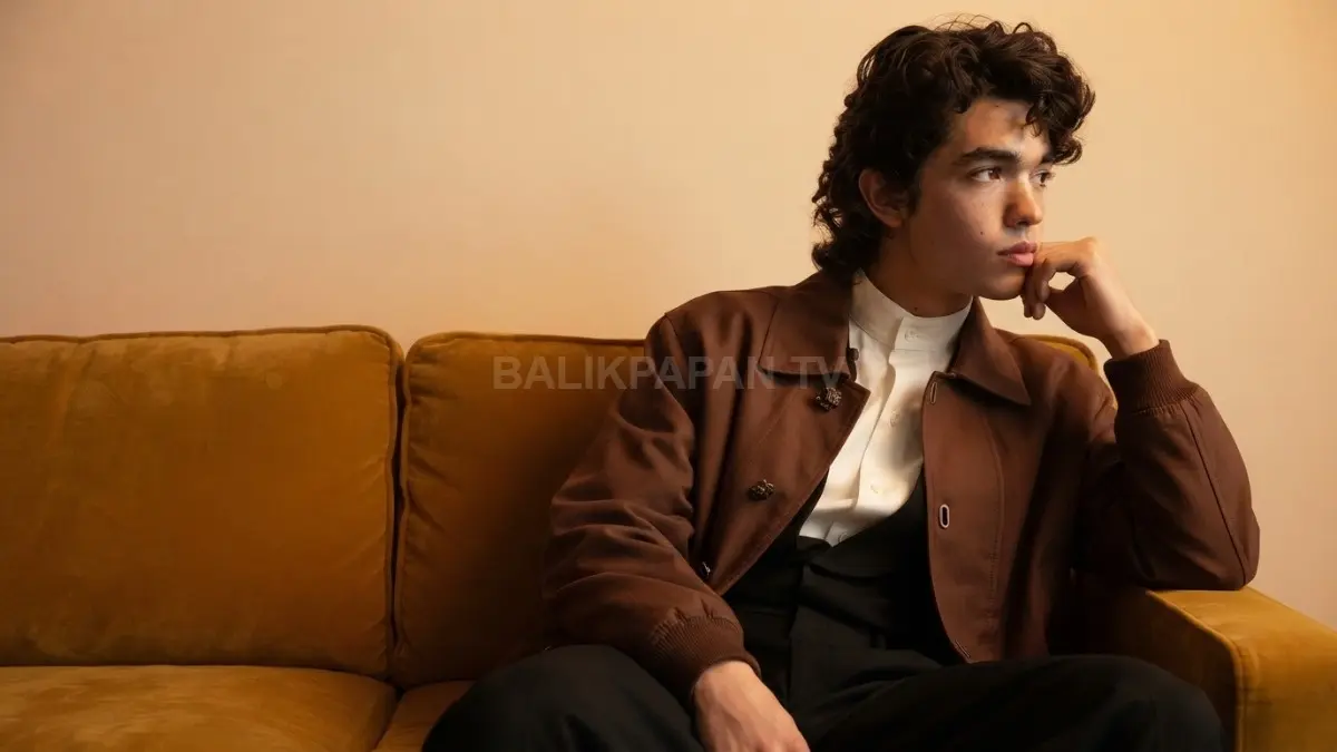 Potret estetis Conan Gray berbusana cokelat sedang duduk menopang dagu di atas sofa. (BTV/Ai)