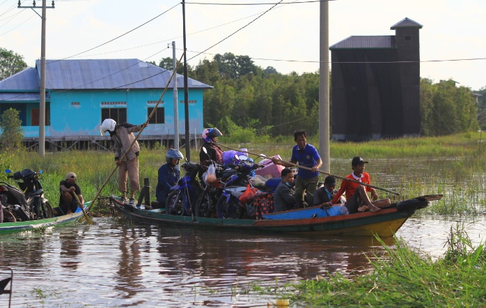 DENAR/KALTENG POS NAIK PERAHU: Pengendara roda dua menumpangi perahu agar bisa melewati banjir di Bukit Rawi.