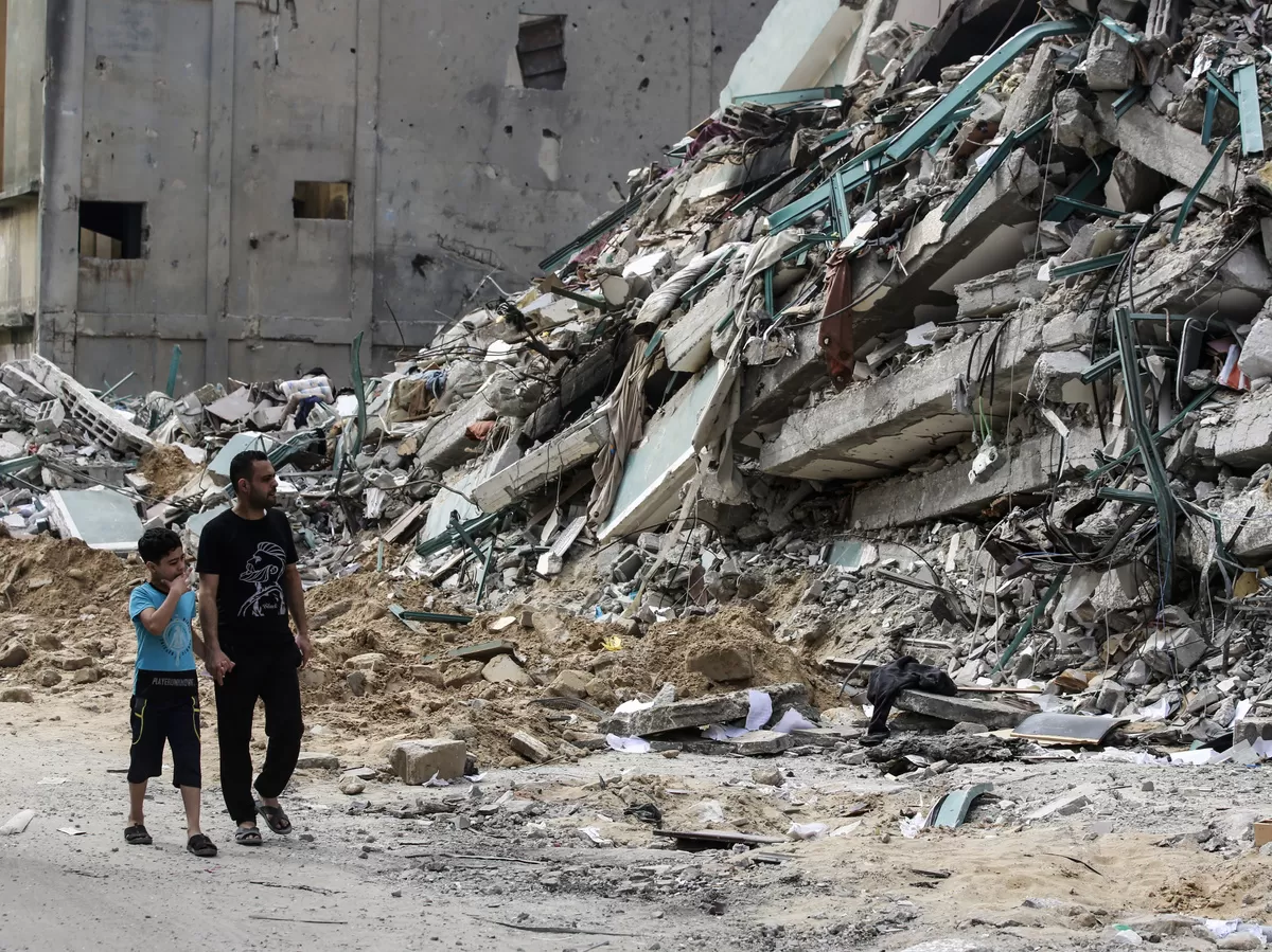 Warga Palestina berjalan melewati menara yang hancur setelah 11 hari pertempuran mematikan yang menghantam Gaza dan memaksa banyak warga Israel mencari perlindungan dari roket. (SOPA Images)